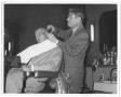 Primary view of [Lamar Fleming, Jr. cutting unidentified man's hair in barber chair]