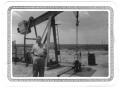 Primary view of [Lamar Fleming, Jr. posed in front of oil well with sign L. F. Oil Co.]