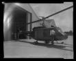 Primary view of [Photograph of individuals rolling a YUH-1D Iroquois helicopter out of a large aircraft hangar, 2]
