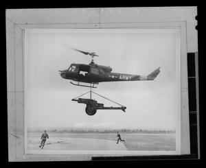 Primary view of object titled '[Photograph of a UH-1B Iroquois helicopter carrying a piece of equipment]'.