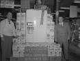 Primary view of [Two Men Standing Next to a Refrigerator and Bags of Flour]