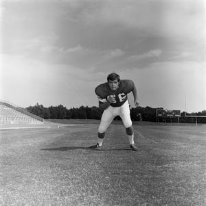 Primary view of object titled '[Football player #56, George Bray, running in a crouched position framed by a stadium field]'.