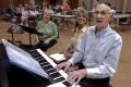 Photograph: [Bob Rogers playing piano with people seated behind him]