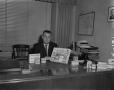 Photograph: [Man at desk posing with Bristol-Myers products for telelog]