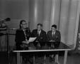 Photograph: [Men seated at table with microphone]