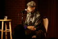 Photograph: [Photograph of Melvin Van Peebles sitting in a chair on a stage]