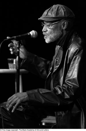 Primary view of object titled '[Photograph of Melvin Van Peebles on stage with a microphone]'.
