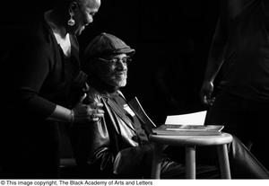 Primary view of object titled '[Photograph of a woman standing behind Melvin Van Peebles on stage]'.