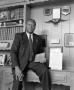 Photograph: [Dr. Norman E. Dyer leaning against his desk and holding a report #2]