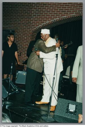 Primary view of object titled '[Photograph of Albert Lipscomb hugging another man with Sandra Kaye in the background]'.
