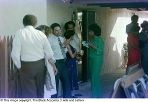 Primary view of object titled '[Photograph of a fenced area near a garage where groups of people are standing around]'.