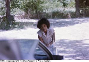 Primary view of object titled '[Photograph of a woman leaning towards the trunk of a vehicle]'.