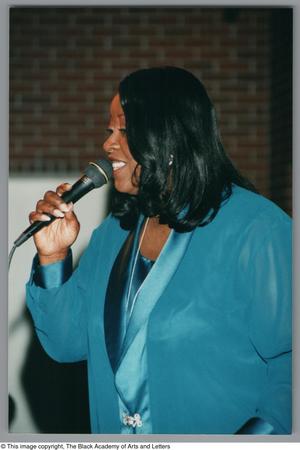 Primary view of object titled '[Photograph of a woman singing into a microphone facing towards the left]'.