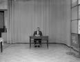 Photograph: [Man sitting at a desk on a tv set]