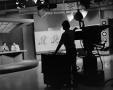 Photograph: [Photograph of camera operators silhouette filming news team on set]