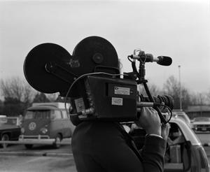 Primary view of [Photograph of an individual standing in a parking lot with a camera]