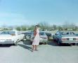 Photograph: [Debby Herman posing in front of cars]