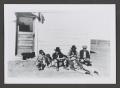 Photograph: [Photograph of individuals in hats sitting outside a house]