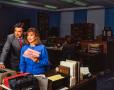 Photograph: [Photograph of Jane McGarry and a man posing at a desk, looking to th…