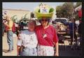 Photograph: [Janie Bush with a crew member in a large green hat and rainbow wig: …