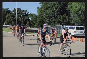 Primary view of object titled '[Two lines of cyclists ride through a parking lot: Lone Star Ride event photo]'.