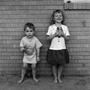 Photograph: [Two children standing in front of a brick wall #1]