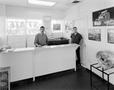 Photograph: [Two men standing behind a counter at a mechanic shop]