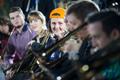 Photograph: [Four people in a row turning to look at brass musicians performing]