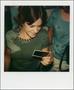 Photograph: [Woman in a crowd holding a polaroid]