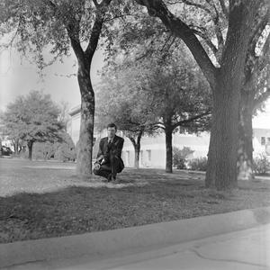 Primary view of object titled '[Male Who's Who student kneeling beside a tree]'.