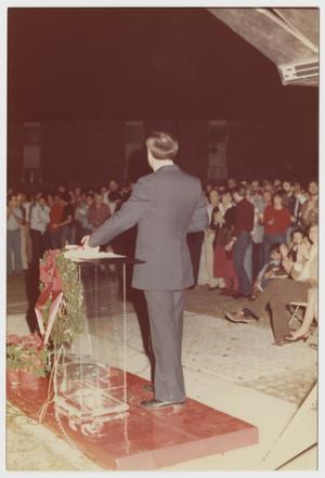 Primary view of object titled '[Don Baker with his back facing camera standing in front lectern]'.