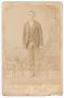 Photograph: [Unknown Young Man Standing Next to Wooden Chair]