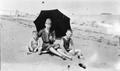 Photograph: [Three People Sit With an Umbrella at the Beach]