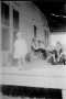 Photograph: [A group of people sitting on a porch, child standing near the edge o…