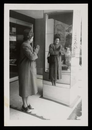 Primary view of object titled '[Sheila Emery Allen looking at her reflection in mirror near storefront]'.