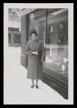 Primary view of object titled '[Sheila Emery Allen standing in snow next to storefront window]'.