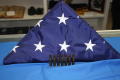 Photograph: [Image of a triangular folded U.S. Flag and seven shell casings]
