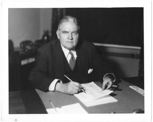 Primary view of object titled '[George A. Hill, Jr. behind desk with papers]'.