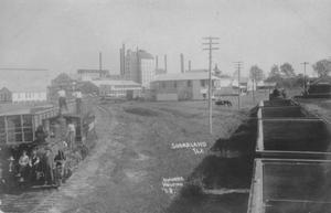 Primary view of object titled '[Sugar Mill and railroad cars, men are standing on the train engine to the left]'.