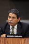 Photograph: [Michael Hinojosa sitting at table with nameplate and microphone]
