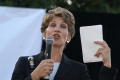 Photograph: [Laura Miller holding white papers and microphone]