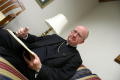 Photograph: [Bishop Kevin Vann sitting on sofa with book and pen]