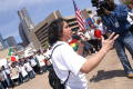 Photograph: [Speaker is filmed by cameraman in front of protesters]