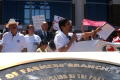 Photograph: [Speaker with a microphone, waving his arm, and protesters behind him]