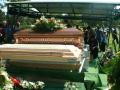Photograph: [Casket and flowers with mourners in background]