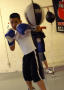 Photograph: [Two students practicing hitting bags while wearing boxing gloves]