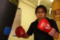 Primary view of [Young woman in red boxing gloves surrounded by three heavy bags]
