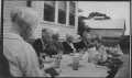 Photograph: [Women eating lunch at a table set up in a yard.]
