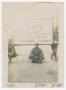 Photograph: [William Giannopoulos Sitting Under a Sign Denoting the Italian Borde…