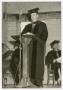 Photograph: [Man Wearing a Cap and Gown Behind a Lectern]